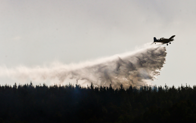 A plane drops flame retardant to extinguish a fire in Chile’s Tambotinaja community, Thursday, Feb. 2, 2017. Image: AP Photo/Esteban Felix